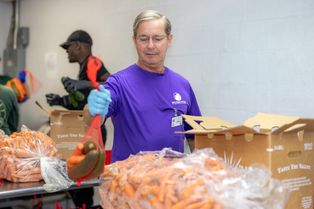A volunteer beams while holding a whole watermelon at the HCFB warehouse