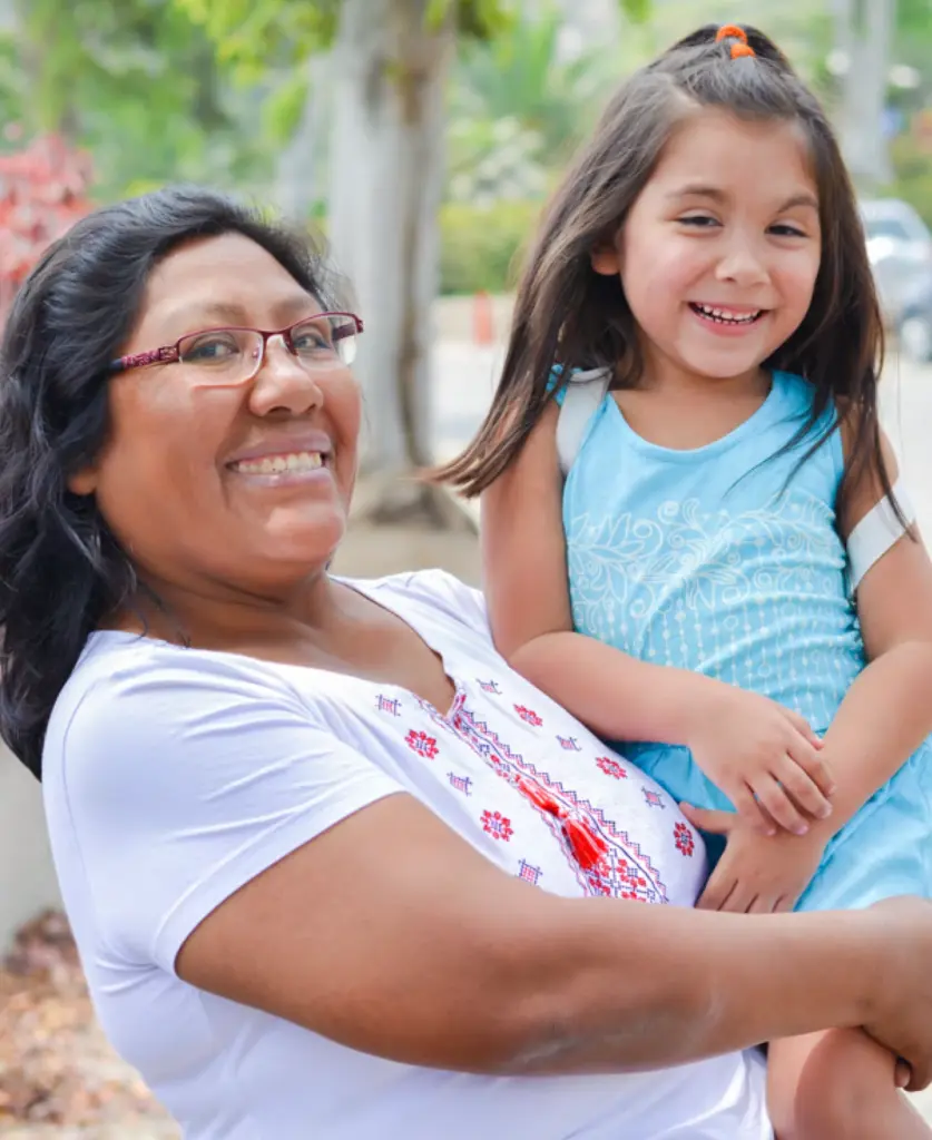 A parent holds a smiling child outdoors.