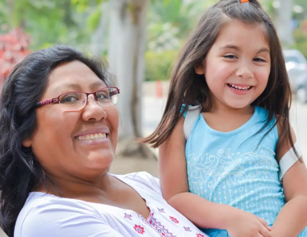 A parent holds a smiling child outdoors.