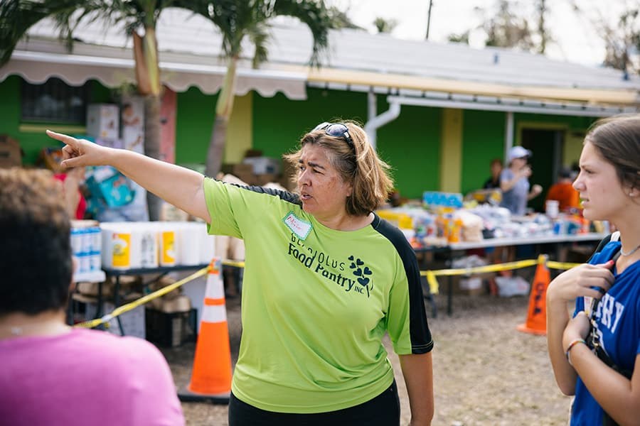 A volunteer in a partner food pantry T-shirt gesturing and directing activity at an outdoor distribution site.