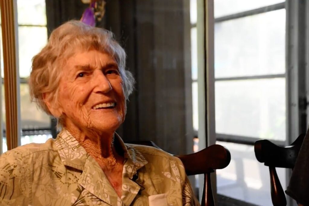 An older adult smiling warmly while seated indoors.