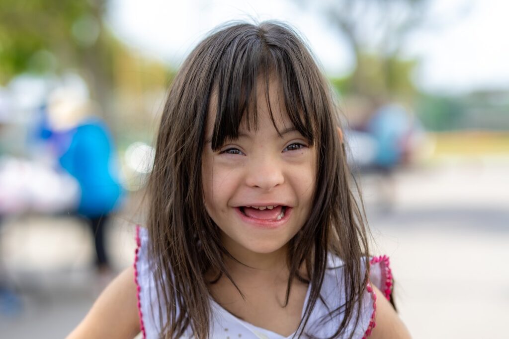 A smiling young child with a milk carton, photographed outdoors at a food distribution site.