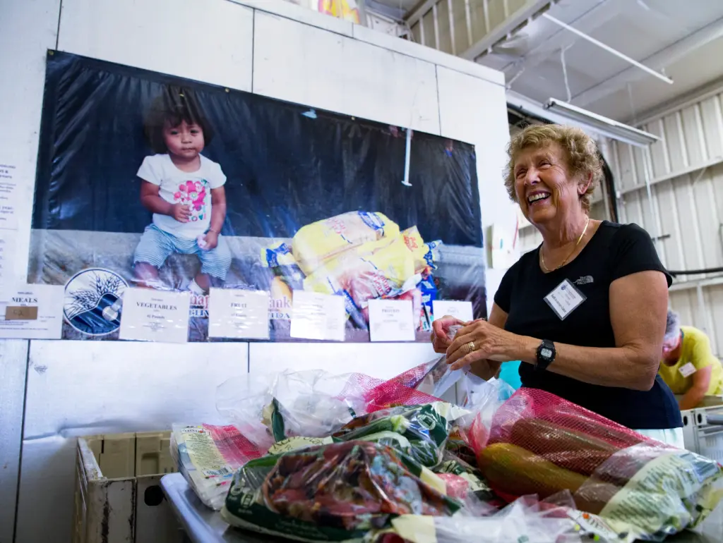 A smiling volunteer sorts bags of fresh produce in a warehouse.